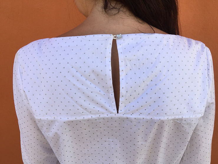 gros plan de l'ouverture dos de la blouse myraj cousue en coton blanc à pois fermée par un bouton